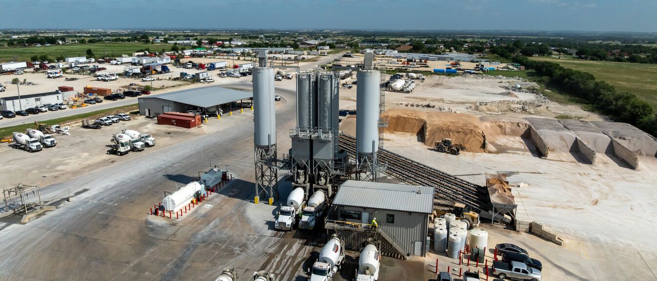 Concrete batch plant from altitude — silos, mixer fleet, and material yard