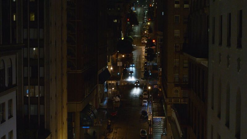 Night street canyon from above, headlights threading the grid